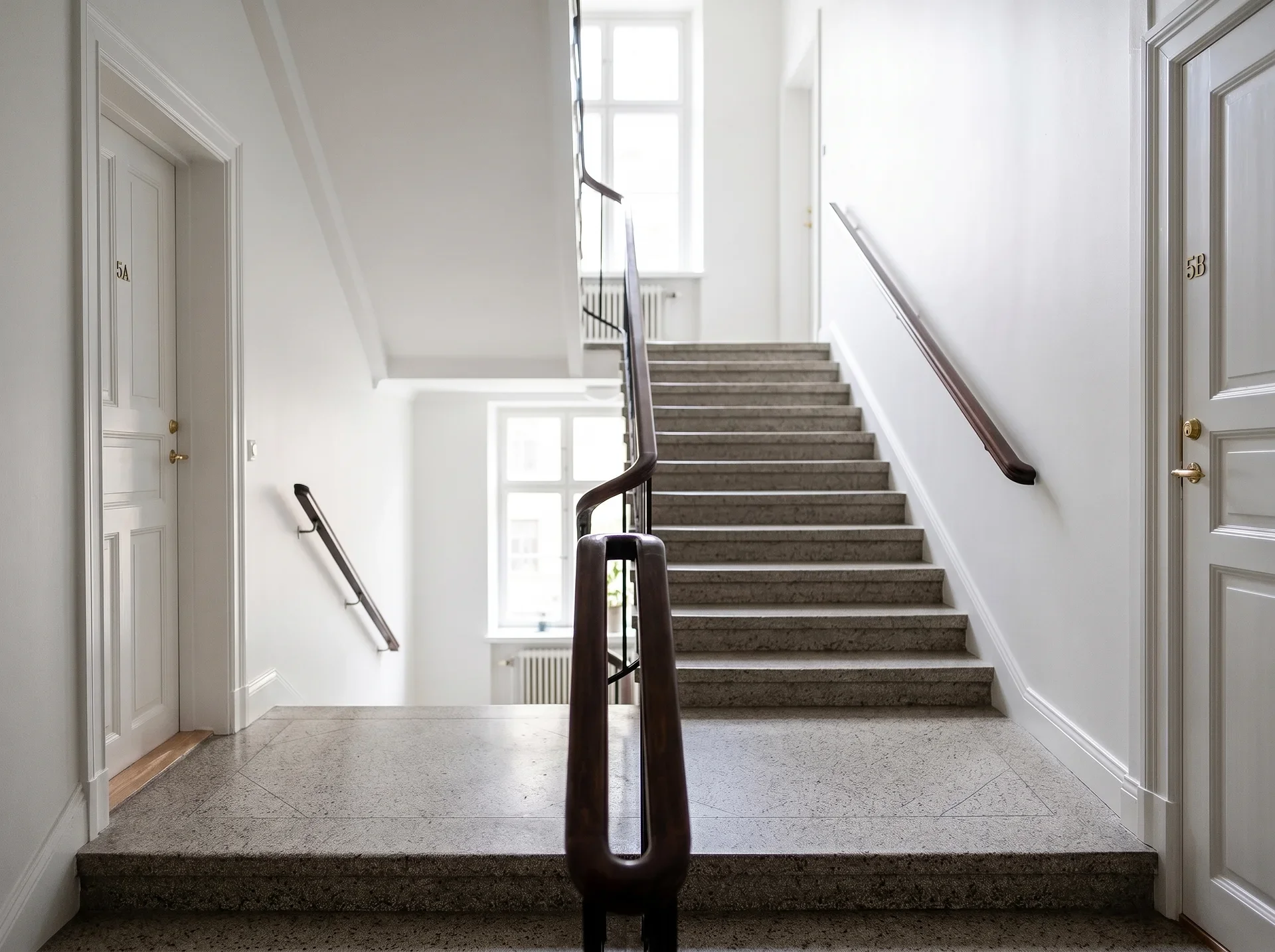 Ljust trapphus med stenstrappa, vita dörrar märkta 5A och 5B.