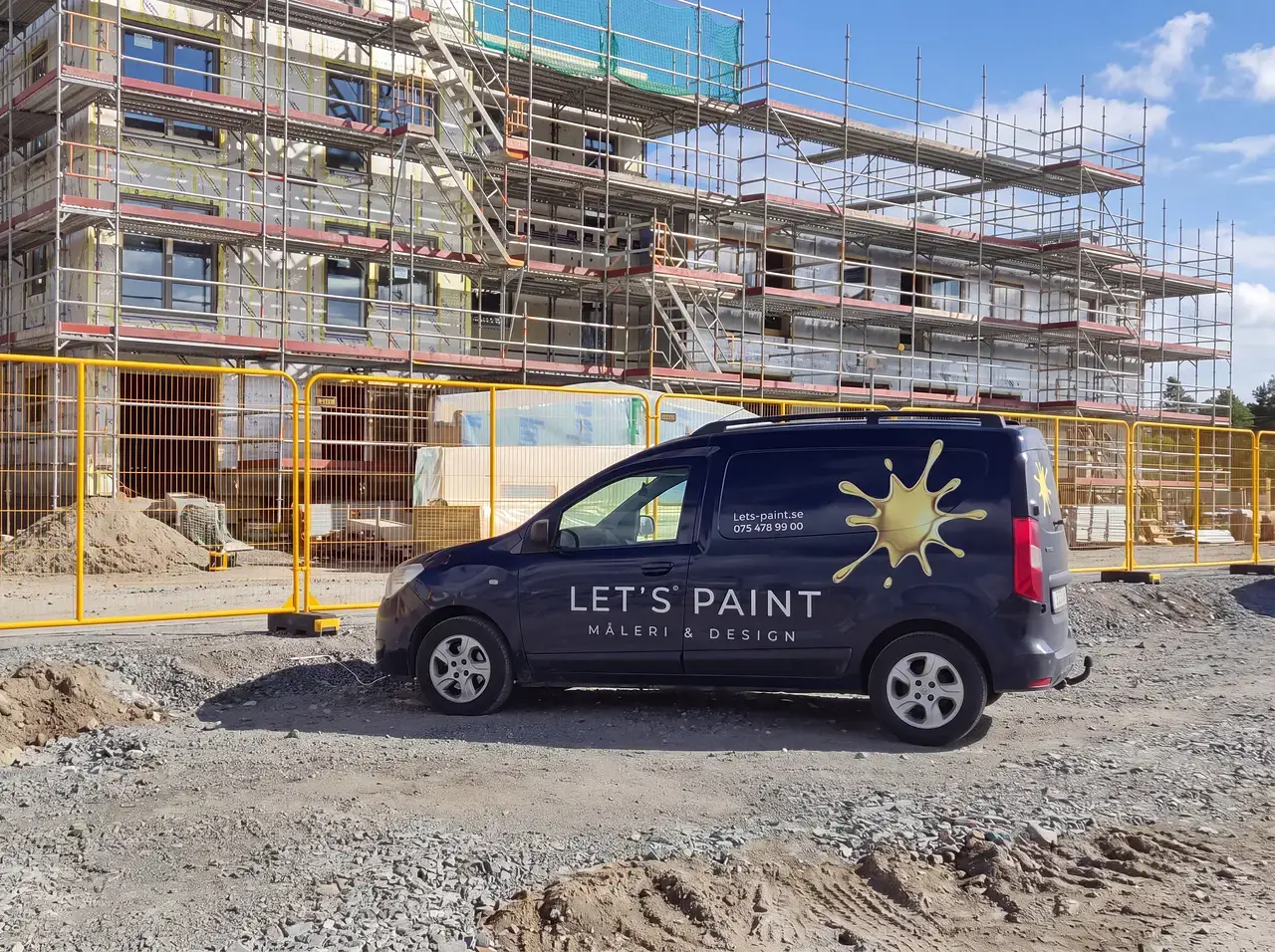 Mörkblå skåpbil med "Let's Paint"-logotyp framför byggarbetsplats med ställningar.